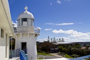 Small white lighthouse in front of suburban housing and blue skies.