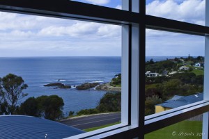 View through rectangular aluminium-framed windows, of coastline with rocky outcrops.