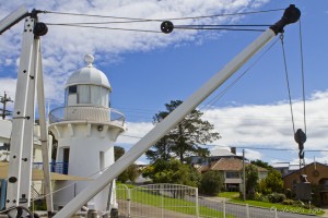 White derrick crane in front of a small white lighthouse.