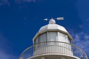 Top of a white lighthouse with a white wind vane.