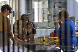 Reverse view from a striped mirror: a family examining scrimshaw on a glass counter.