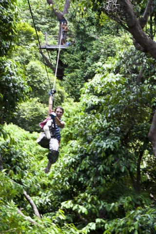 Laughing woman on a cable hipline over jungle