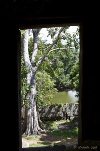Through the doorway of an Angkok style ruin to a green pond.