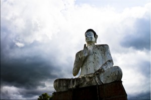 Giant white seated buddha state against a cloudy sky.