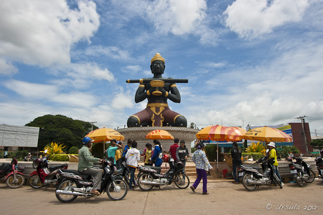 Large  statue of a Khmer King with a large stick sits in a central circus in Battambang.