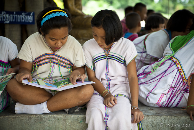 Young Karen girls in traditional dress reading under a tree.