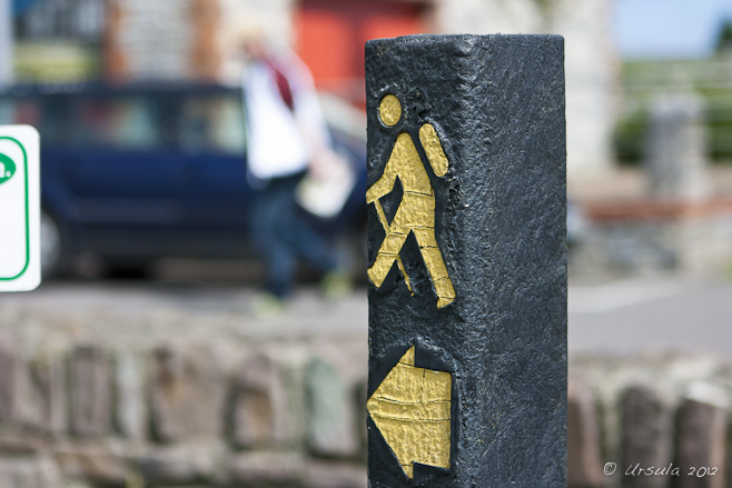 Yellow walking man on a black signpost.