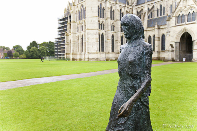 Sculpture of a woman walking on the green grass in front of Salisbury Cathedral.