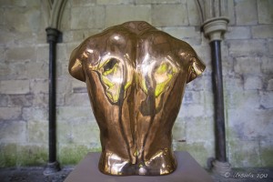 Gold sculpture of the back of a male torso.