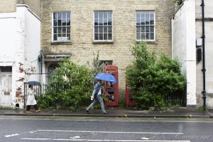 Two people with umbrellas walking on a British street.