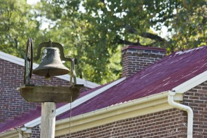 Brass bell against a red roof.