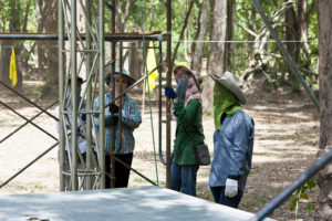 Three Thai workers in hats and long sleeves steady a scaffolding.