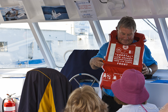 Gray haired man demonstrating a safety floatation device on a boat.