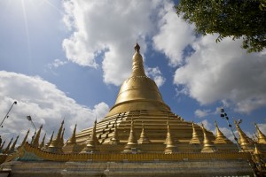 The golden Shwemawdaw Temple in afternoon light against fluffy white clouds.