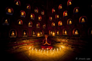 Young burmese monk surrounded by candle-lit alcoves with Buddhas in them,