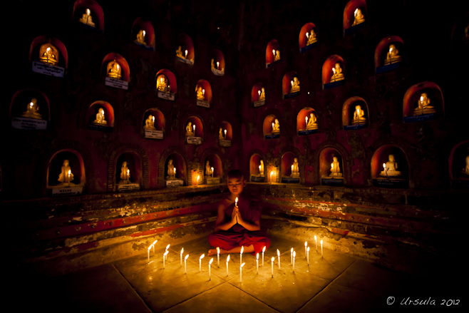 Young burmese monk surrounded by candle-lit alcoves with Buddhas in them, Shweyanpyay Monastery, Naung Shwae, Myanmar