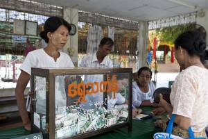 Burmese people with a glass case containing money in exchange for prayer papers.