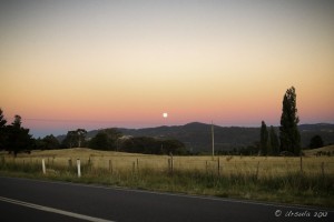 Full moon rising through an orange sky over fields and low mountains. Jindabyne, NSW