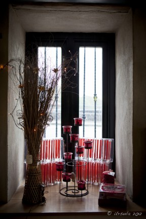 Red candle holders  and a vase of black reeds inside a black-framed window.