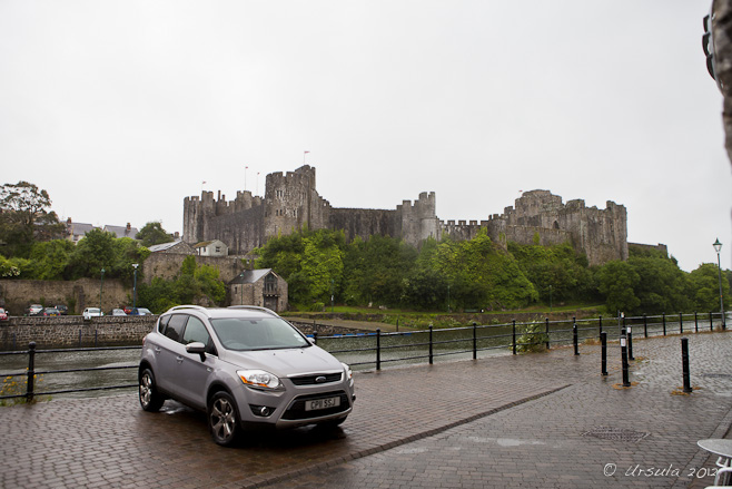 Pembroke Castle against a rainy sky; a parked car and the River Cleddau.