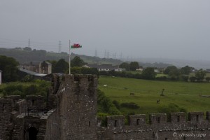 The Welsh flag flies from a Pembroke Castle tower; against rainy skies and green fields.