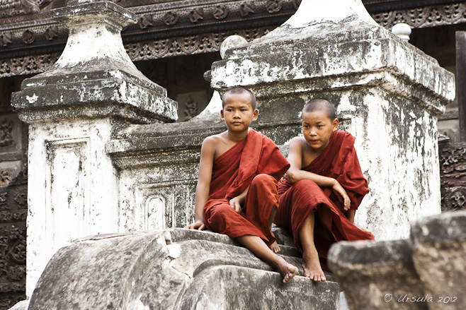 two young novice monks in maroon robes sitting on the stairs of Shwenandaw Monastery, Mandalay.