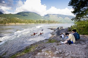 Landscape: people sitting on a rock overlooking kayaks on Sechelt Rapids.