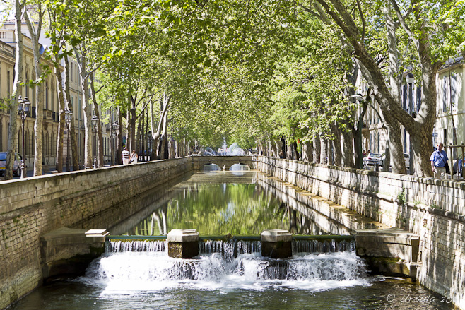 A canal with water wheels under an avenue of trees, Nîmes, France.