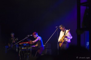 Dark blue stage: Shuggie Otis, spotlit on guitar, pianist in background