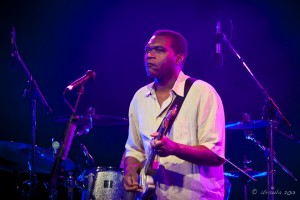 Portrait: Robert Cray in blue and pink light, on guitar.