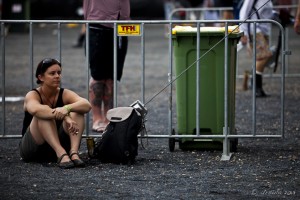 Young woman sitting on the gravel against a fence barricade, Bluesfest 2013