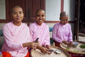 Three burmese nuns in pink robes and red skirts, sitting on a bench, preparing food, Sagaing Hill
