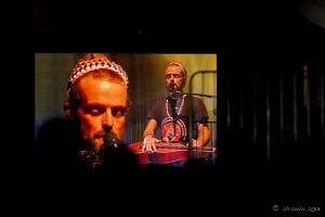 Screenshot: Two headshots of Xavier Rudd on didgeridoos and guitar