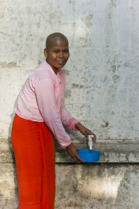 Portrait of a smiling burmese nun drawing water from a tap, Sagaing Hill