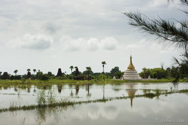 A white burmese Chedi under a white sky, reflected in flooded Rice patties, Inwa Island, Myanmar