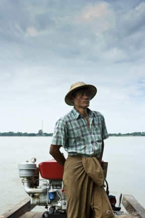 Burmese male in a pith hat and check shirt steering a motorboat Irrawaddy River