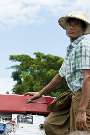 Burmese male in a pith hat and check shirt steering a motorboat Irrawaddy River.