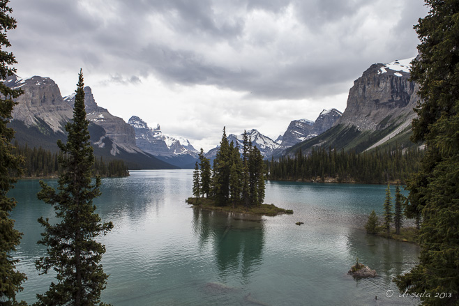 Landscape: snow capped mountains and little treed island reflected in the still waters of Maligne Lake