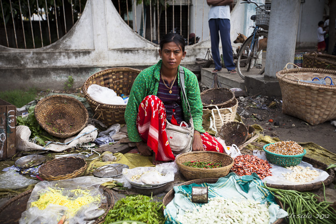 A Burmese woman sits on the ground in a street market, surrounded by her beans.