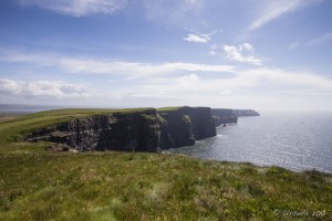 Landscape: the curving south end of the Cliffs of Moher under a blue sky.