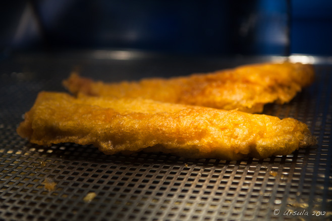 Two pieces of battered fish on a fryer drainboard, Brighton, UK