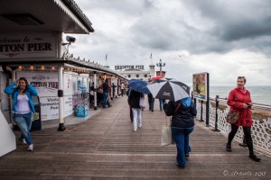 People on a wet Brighton Pier, in raincoats and under umbrellas, Brighton, UK