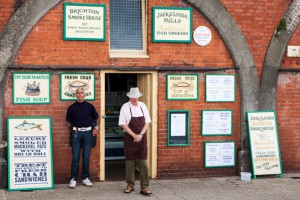 Two men outside one of the Victorian fishermen's workshops, now a smokehouse store, Brighton Beach, UK