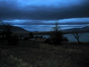 Dark blue morning light over a house and trees on a lake, Glacier National Park, Argentina
