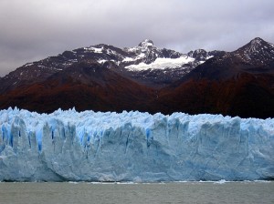 A wall of glacier seen from Lake Argentino, mountains behind.