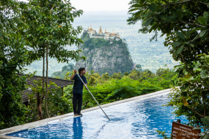 A burmese man cleans a pool, Mount Popa in the background, Myanmar