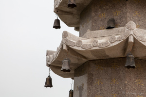 Smal bells on a stone pagoda against a tray sky, Jinjiang, China