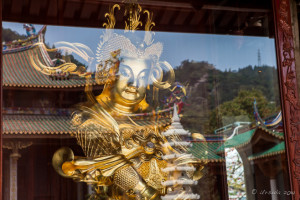 A golden Chinese guardian with the reflection of temple buildings, a white Longevity Tower, and Wulaofeng; Five Old Men Mountain, Xiamen