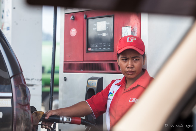 Indonesian woman in a red uniform pumping gas.