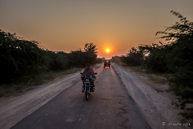 A motorcycle and a jeep on a narrow road against the Sunrise, Rajasthan India